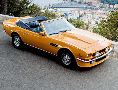 Classic golden convertible sports car parked on a scenic overlook with a coastal city in the background.