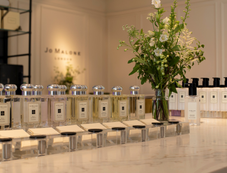 A sophisticated arrangement of Jo Malone perfume bottles on a marble countertop, accompanied by a vase of fresh flowers, creating an elegant and luxurious ambiance in the store.