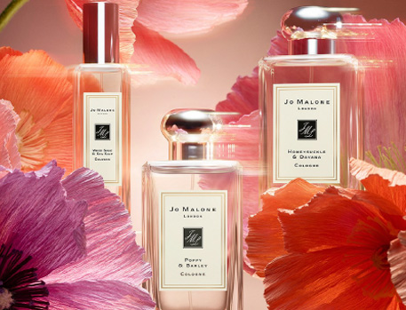 Close-up of Jo Malone perfume bottles surrounded by vibrant, colourful flowers, highlighting the elegance and botanical inspiration behind the fragrance collection.