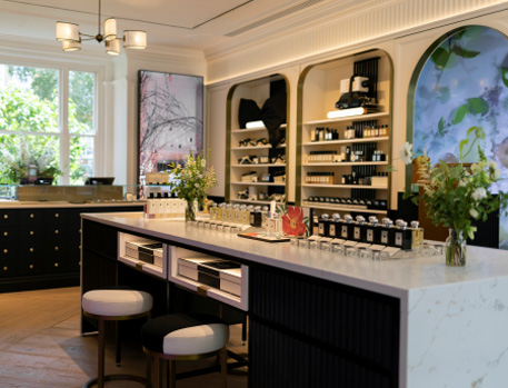 Elegant interior of a luxury fragrance boutique featuring a marble counter with perfume displays, stylish shelving units, and a cosy seating area, all set against a backdrop of artistic wall decor and natural light from large windows.