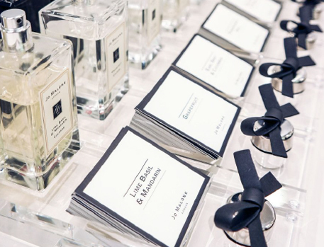 Close-up of Jo Malone perfume bottles accompanied by neatly arranged tester cards and small ribbon-tied perfume samples, providing a detailed view of the fragrance selection.