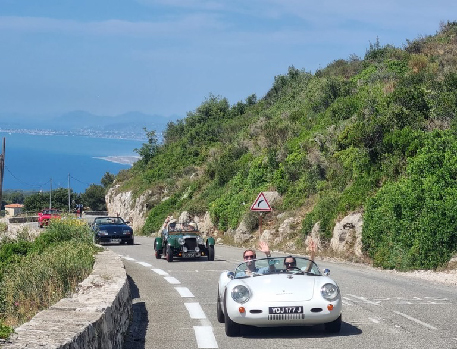 Classic cars driving along a winding mountain road with the coastline visible in the distance.