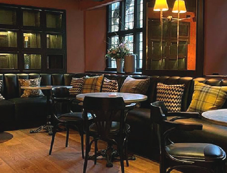 Cosy lounge area with dark leather seating, wooden tables, patterned cushions, and warm lighting.