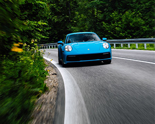 The image features a vibrant blue sports car in motion on a scenic mountain road, surrounded by lush greenery.