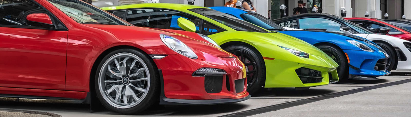 A line-up of vibrant supercars, showcasing a variety of colours including red, green, and blue. The cars are parked in a row, each flaunting distinctive and aggressive designs typical of high-performance sports cars.