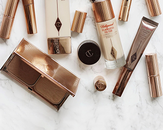 A flat lay of various Charlotte Tilbury makeup products, including foundation, lipsticks, eyeshadow palette, and other beauty items, arranged on a marble surface.