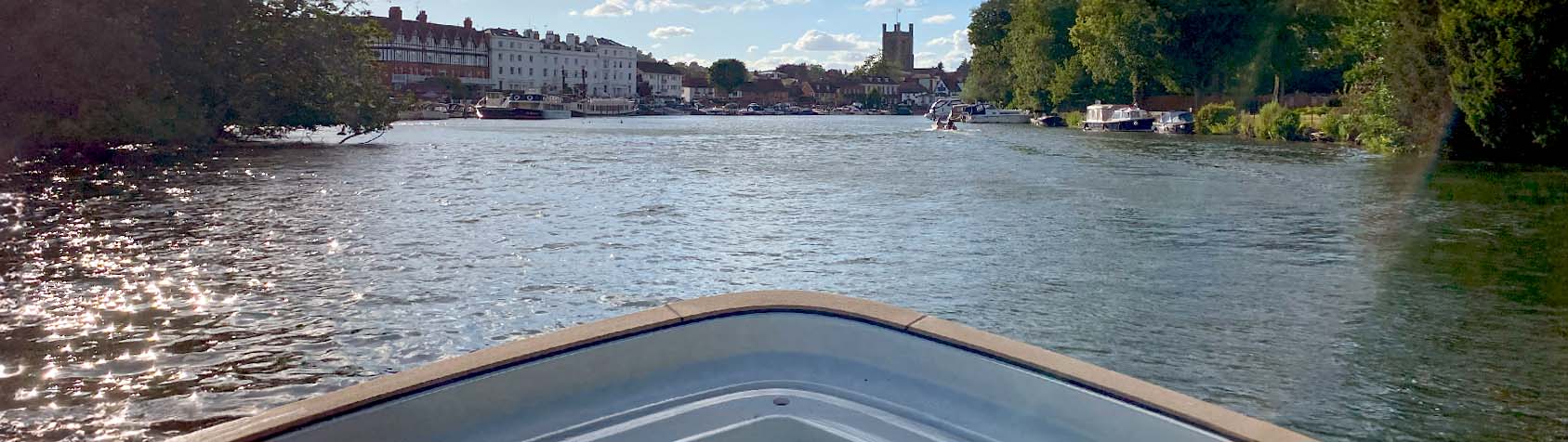 A view from the front of a private boat cruising along the Thames River, approaching the Henley Royal Regatta area.