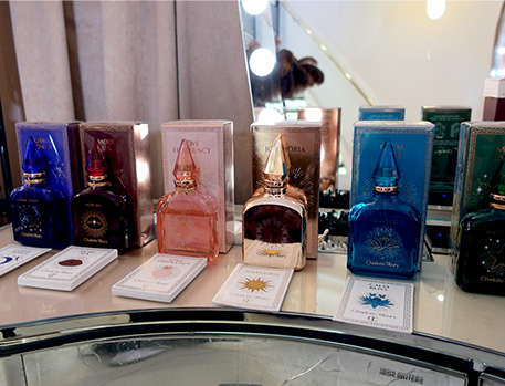 A display of Charlotte Tilbury perfumes in various coloured bottles, each with matching packaging, arranged on a vanity table.