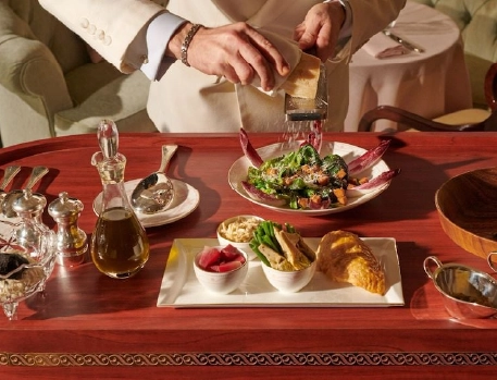 High-end table-side dining experience at The Dorchester, London, showcasing a gourmet salad preparation with fresh ingredients, elegant silverware, and attentive service in a luxurious setting.