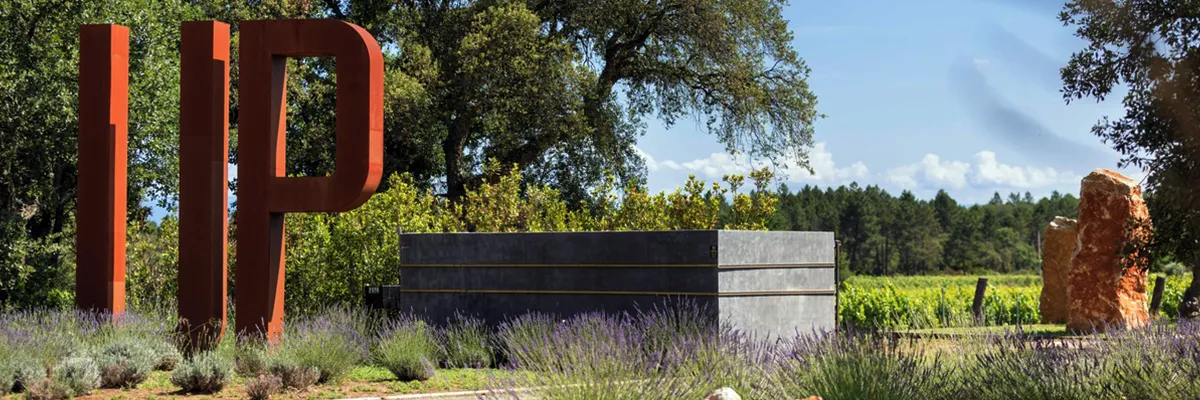 Entrance to Ultimate Provence Hotel surrounded by lavender fields and vineyards, featuring a large "UP" sign with scenic countryside in the background.