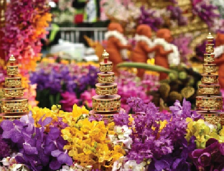 A display of golden pagoda-like decorations amidst a variety of bright purple, yellow, and pink flowers at a floral event.
